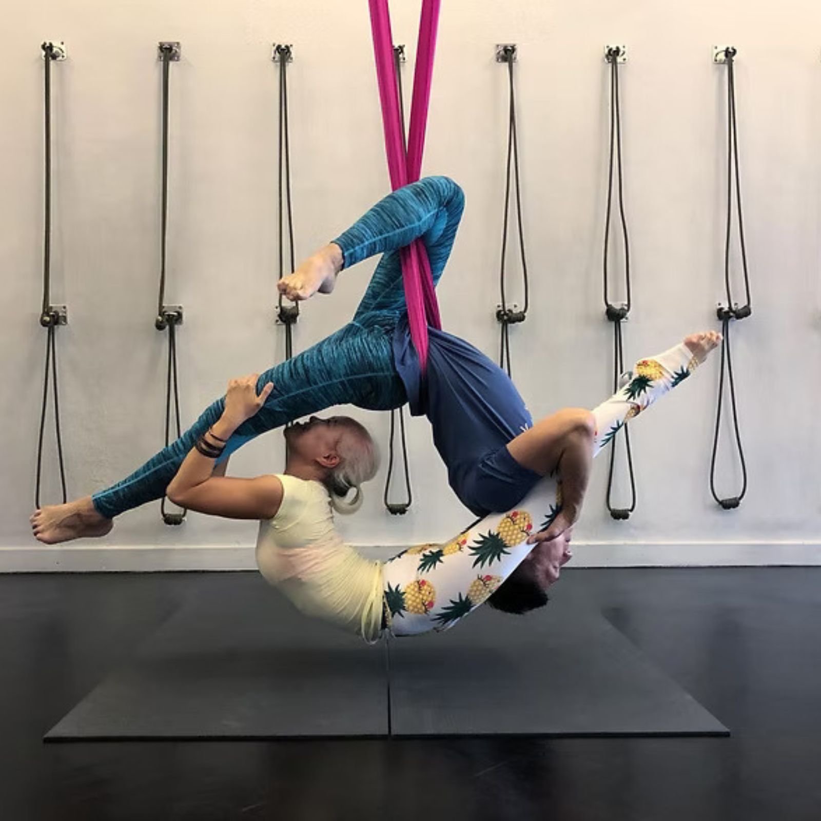 Two people performing aerial silk acrobatics in a studio.