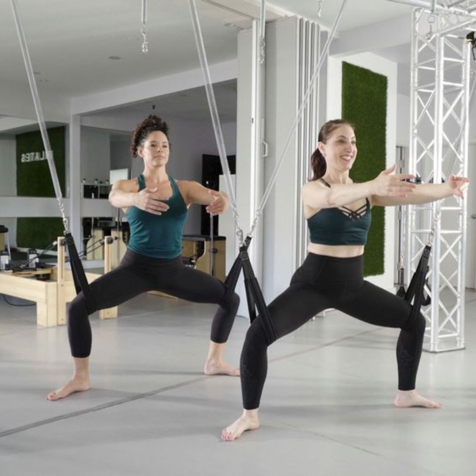 Two people practicing yoga with assistance from suspended straps in a modern studio.